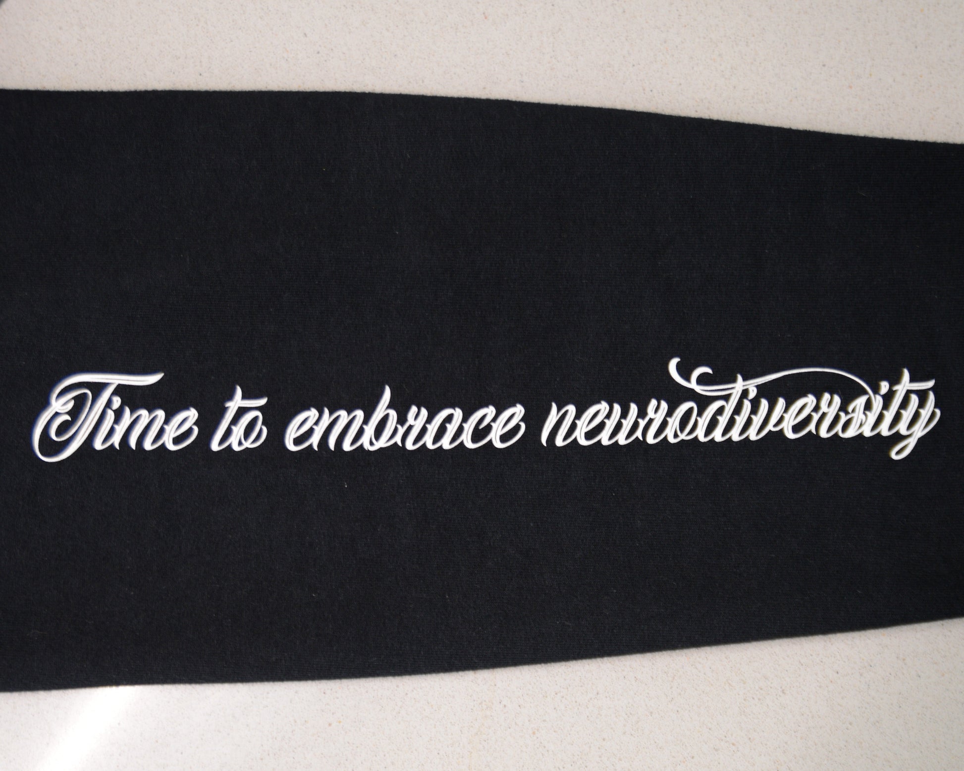 Black ribbon with white text 'Time to embrace neurodiversity' on a white background